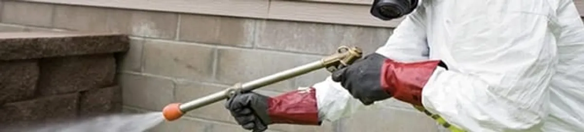 Pest control technician applying exterior insect treatment along a home foundation in Bradenton, FL