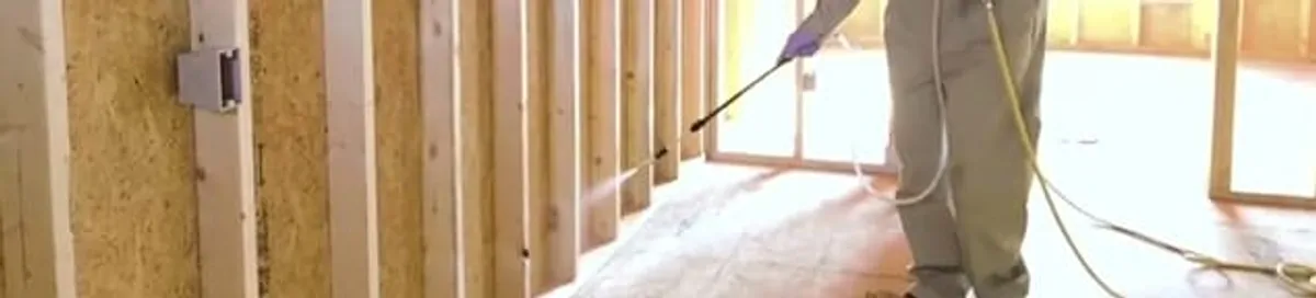 Termite treatment technician applying spray along framing and unfinished walls in Bradenton, FL